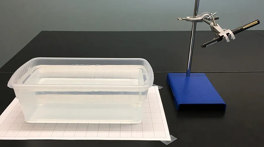 Setup for demonstration showing a small tub of water next to a small laser pointer held by a clamp