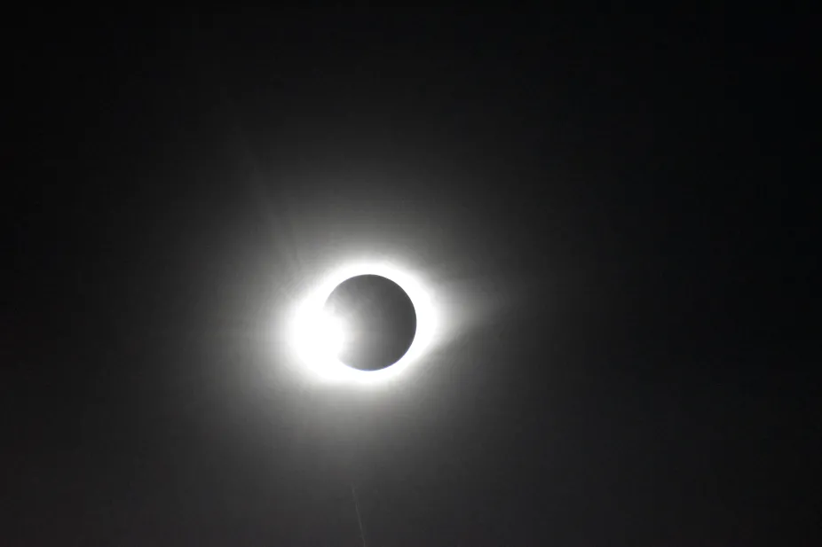 The 2019 solar eclipse, captured in-flight from the NSF Gulfstream - V aircraft. The Moon appears as a dark marble with a bright halo of light surrounding it. On the left side the Sun is peaking out. 